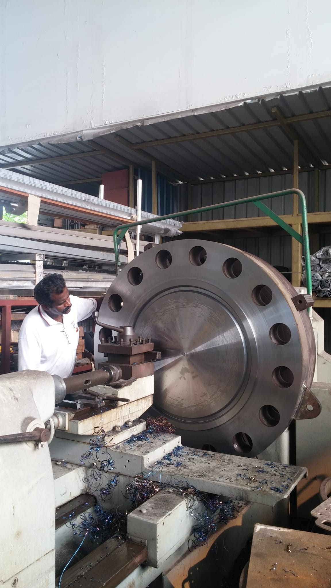 Worker beside a large circular flange mounted on a lathe